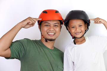 A joyful asian father and son wearing helmets, pointing to their helmet, celebrating safety and fun together.