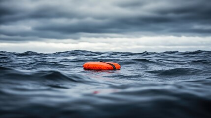 Fototapeta premium Bright orange life buoy floating alone in dark, choppy ocean waters under a cloudy sky, symbolizing safety and survival in perilous situations at sea