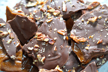 Making chocolate toffee bark with fresh roasted pecans for dessert. Candy bark made of toffee, chocolate and nuts broken up into pieces.