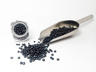 Black plastic masterbatch, polymer carries colorful pigments with small scoops poured into a white...