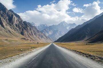 Fototapeta premium Scenic mountain road stretching to majestic snow-capped peaks under a partly cloudy sky.