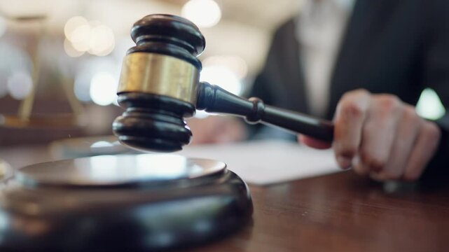 A man is holding a gavel and writing on a piece of paper. The gavel is on a wooden surface and the man is wearing a suit. Scene is serious and formal - Powered by Adobe
