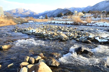 Snow-Covered Riverbank with Distant Mountains and Buildings at Sunset Time, Nagano, Japan