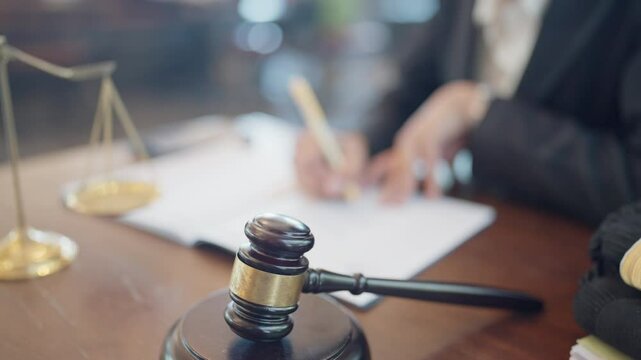 A judge is writing on a piece of paper with a gavel on the table. The gavel is made of wood and has a gold handle