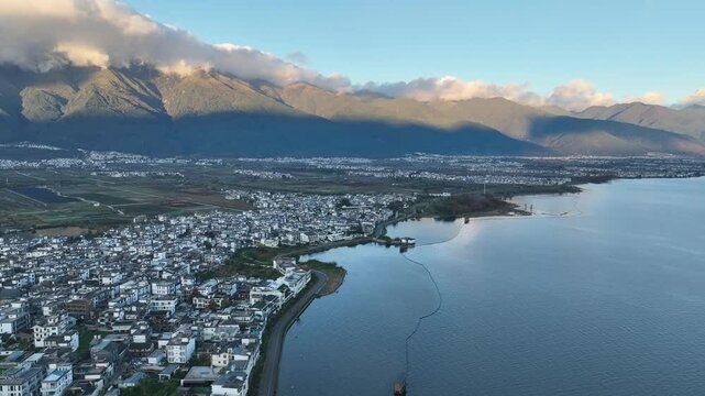 Stunning 4K aerial view of Erhai Lake in Dali, Yunnan, China.  A picturesque town hugs the shoreline, nestled against majestic mountains.