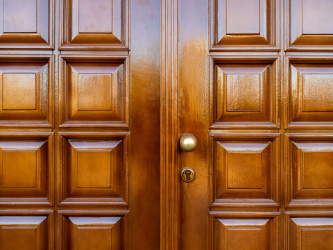 Classic vintage golden brass door knob and keyhole on old and strong of large wood front door, twin doors. Antique knob with square shape pattern, geometric design carvings on lacquer wooden door.