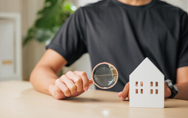 A man hand holds a magnifying glass inspecting a cottage house. Represents real estate appraisal,...