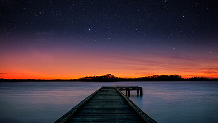 Wooden pier over the blue sea at sunset, dock wallpaper for desktop depicting clouds and starry night sky at dusk digital illustration for pc home screen