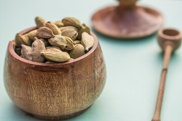 Cardamom in wooden pot on colour background close shot