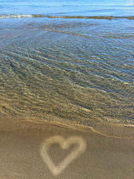 Sea soft waves on the beach with a heart drawn on the sand.