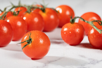 A group of bright, red cherry tomatoes with fresh stems attached, covered in dewdrops.
