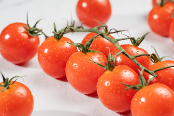 A group of bright, red cherry tomatoes with fresh stems attached, covered in dewdrops.