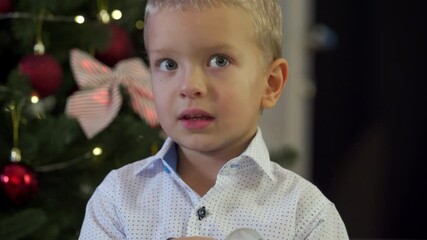 Happy child holding snow globe with figurine of Santa Claus. Smiling face of little boy near Christmas tree. Merry Christmas and Happy New year winter holidays.