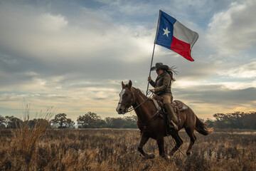Woman Wearing Cowboy Hat Riding Running Horse While Holding Large Texas Flag In Grassy Field With...