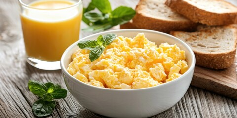 A bowl of fluffy scrambled eggs garnished with mint, accompanied by toast and a glass of fresh juice, creating a vibrant breakfast scene.