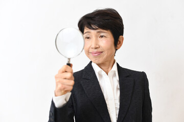 虫眼鏡を持つスーツのアジア人の中高年女性