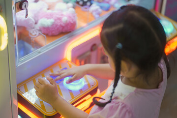 Asian girl playing Claw Game or cabinet catches the doll at one of the shopping mall outlets