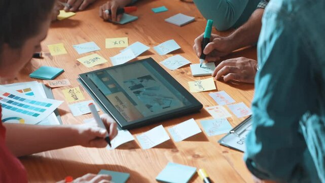 Top view of manager writing idea on sticky notes and explain idea about web design. Professional marketing team or programmer brainstorming idea while looking at tablet with color palette. Symposium.