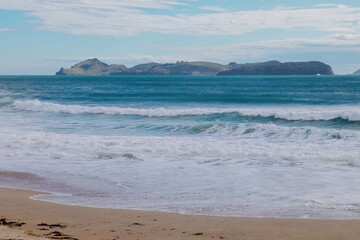 Coastal waves crash on a sandy beach, with distant Slipper islands. Powerful surf. Ocean scene. OPOUTERE, COROMANDEL PENINSULA, NEW ZEALAND