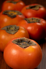 A rustic wooden tray filled with vibrant, ripe persimmons, their orange skin smooth and glossy.