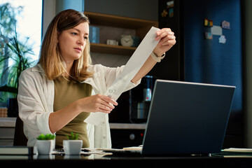 Stressed woman reviewing bills at home. Female organizing receipts, sitting at kitchen table with...