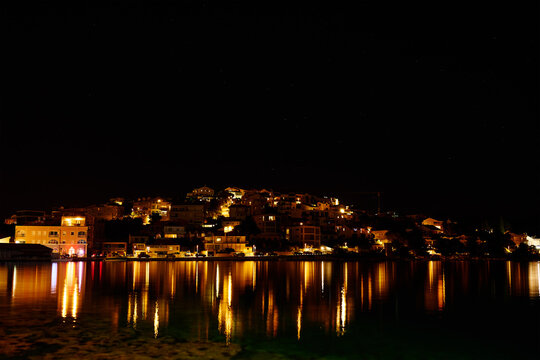 Night view of buildings in coastal town with with evening lights. Illuminated houses of Rogoznica, Croatia with reflection on sea waters under dark night sky