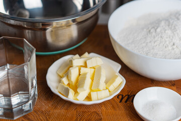 Ingredients for pie dough. Butter sugar flour in white bowl water in glass on wooden cutting board