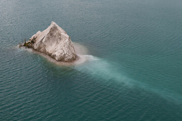 A quarry with blue or turquoise water and a small rocky island, slight waves on the water. Chalk deposits