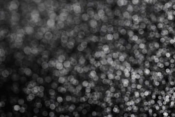 A bokeh background in black and white tones with small particles shining through.