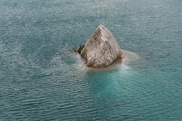 A quarry with blue or turquoise water and a small rocky island, slight waves on the water. Chalk deposits