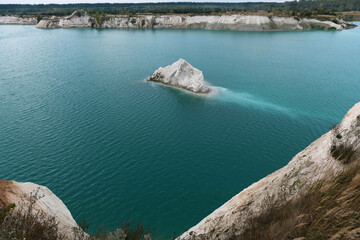 A chalk quarry with blue or turquoise water, steep cliffs and a rocky island