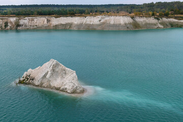 A chalk quarry with blue or turquoise water, steep cliffs and a rocky island