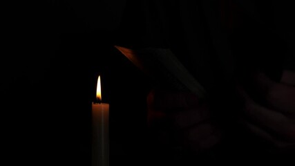 A man sits in dim light, counting dollar bills by the flickering flame of a candle. He faces high utility bills and the stress of rising prices during the energy crisis.