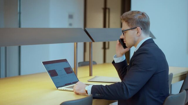 Businessman Manager Sitting with Laptop Picking up Smartphone and Making a Phone Call in Office