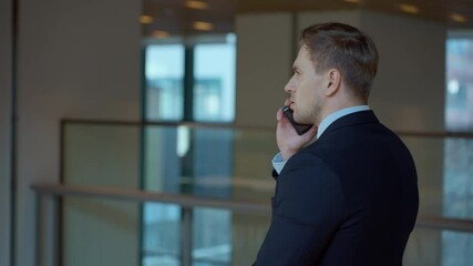 Caucasian handsome businessman in the costume going by the corridor of corporate office and talking on the phone - tracking shot