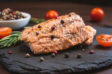 Grilled red fish meat salmon steak with tomato rosemary and spices on black stone background