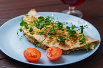 Tasty pork quesadillas with tomato and pea stalks in blue plate on wooden table. Mexican tacos