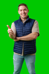 A man in a blue vest stands against a green background