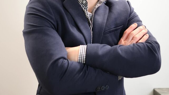 Businessman in a tailored blue suit and checkered shirt stands confidently with arms crossed. A serious expression reflects determination and assertiveness in a corporate environment