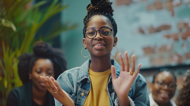 A young Black woman delivering a presentation in an office with her supportive team applauding