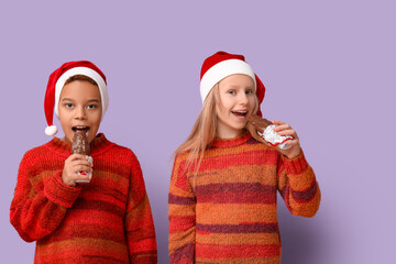 Cute little children eating chocolate Santa Claus on lilac background