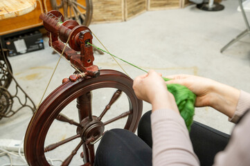 Distaff Day Female caucasian adult spinning yarn with antique spinning wheel in workshop