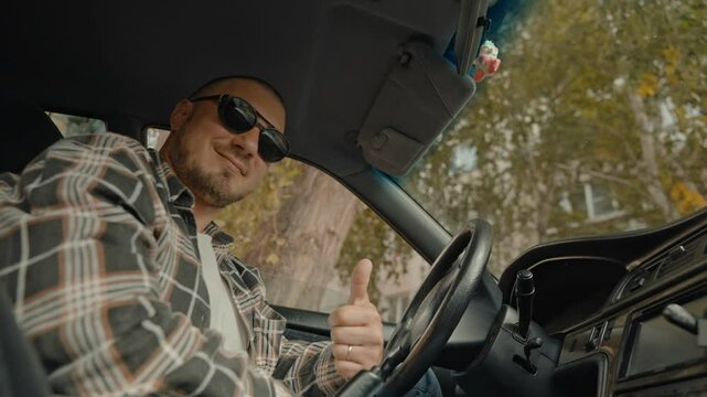 The happy taxi driver gives a thumbs up, smiling affably, takes off his sunglasses and winks with his eye.