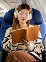 Asian woman sitting on airplane listening to music and writing diary while traveling somewhere during vacation.