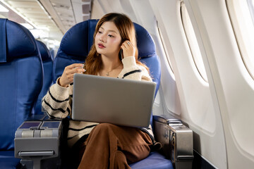 Asian woman sitting watching a movie on her laptop on an airplane while traveling somewhere during her vacation.