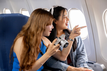 Two happy Asian girls are traveling together. They chat happily and check the photos from the camera during the flight.