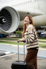 Asian female passenger carrying luggage and walking to board a plane at the airport.