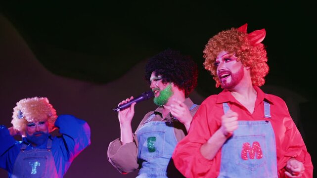 Three drag queens take the stage in vibrant costumes, showcasing their talents and engaging the audience during a lively LGBTQ performance night, filled with music and entertainment.