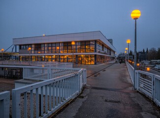 A contemporary train station building captured at dusk, featuring large glass windows reflecting warm interior lighting and glowing street lamps