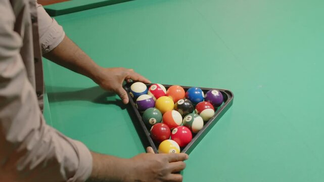 High angle shot of anonymous billiard club worker racking up fifteen colorful balls in triangle pyramid for playing pool game